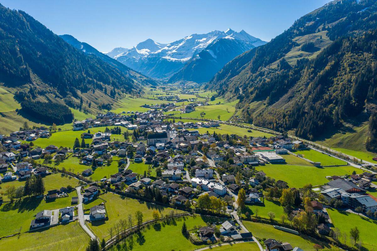 Weitläufige Luftaufnahme eines malerischen Dorfes in einem grünen Tal mit majestätischen Bergen.
