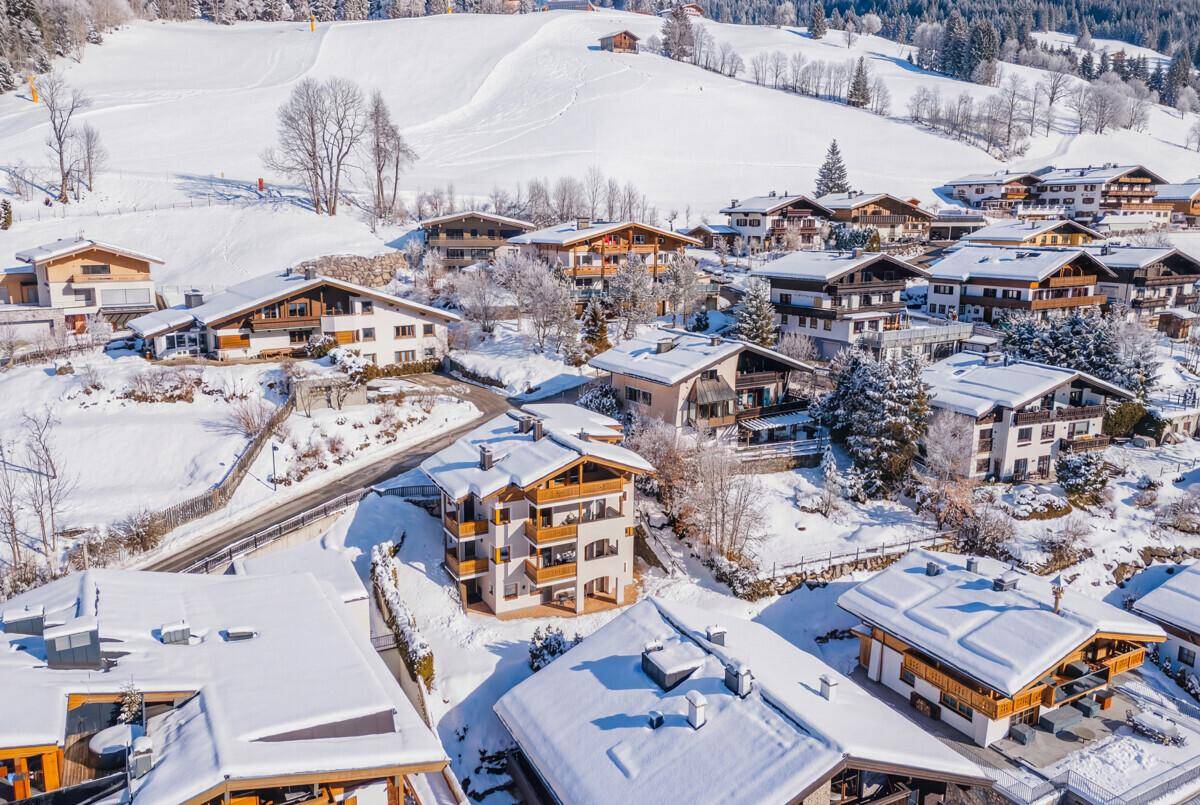 Winterlicher Panoramablick auf ein Alpendorf mit tief verschneiten Häusern und Bergen.