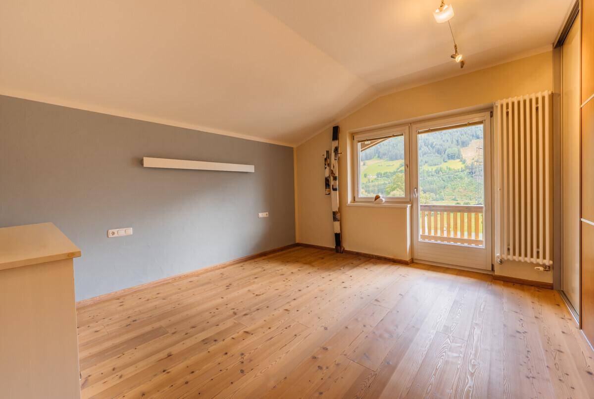 Helles Schlafzimmer mit Holzboden, Dachschräge und Zugang zu einem Balkon mit Bergblick.