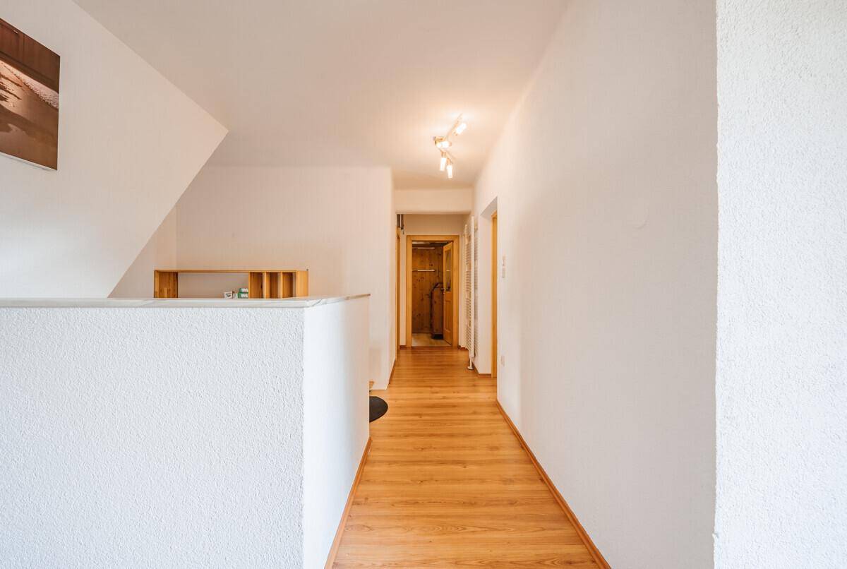 Heller Flur mit Holzboden und weißen Wänden, der zu den angrenzenden Zimmern führt.