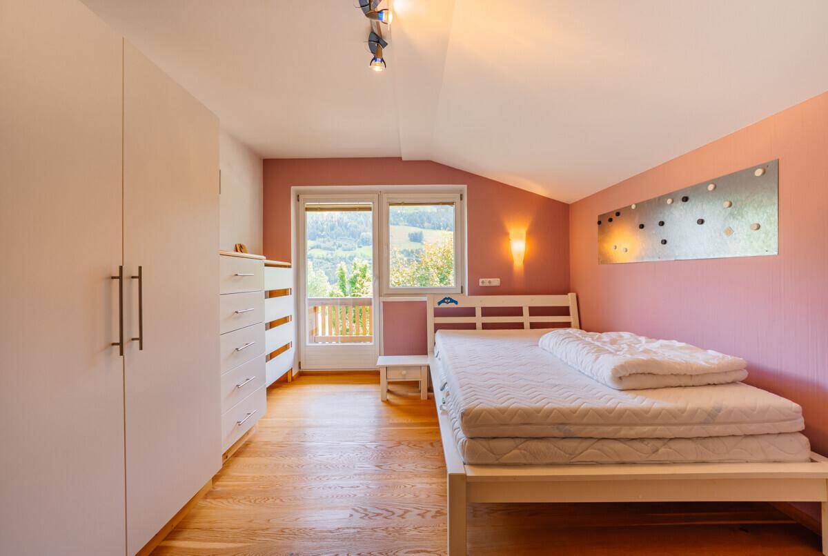 Gemütliches Schlafzimmer mit Holzboden, Dachschräge und rosa Akzentwand.