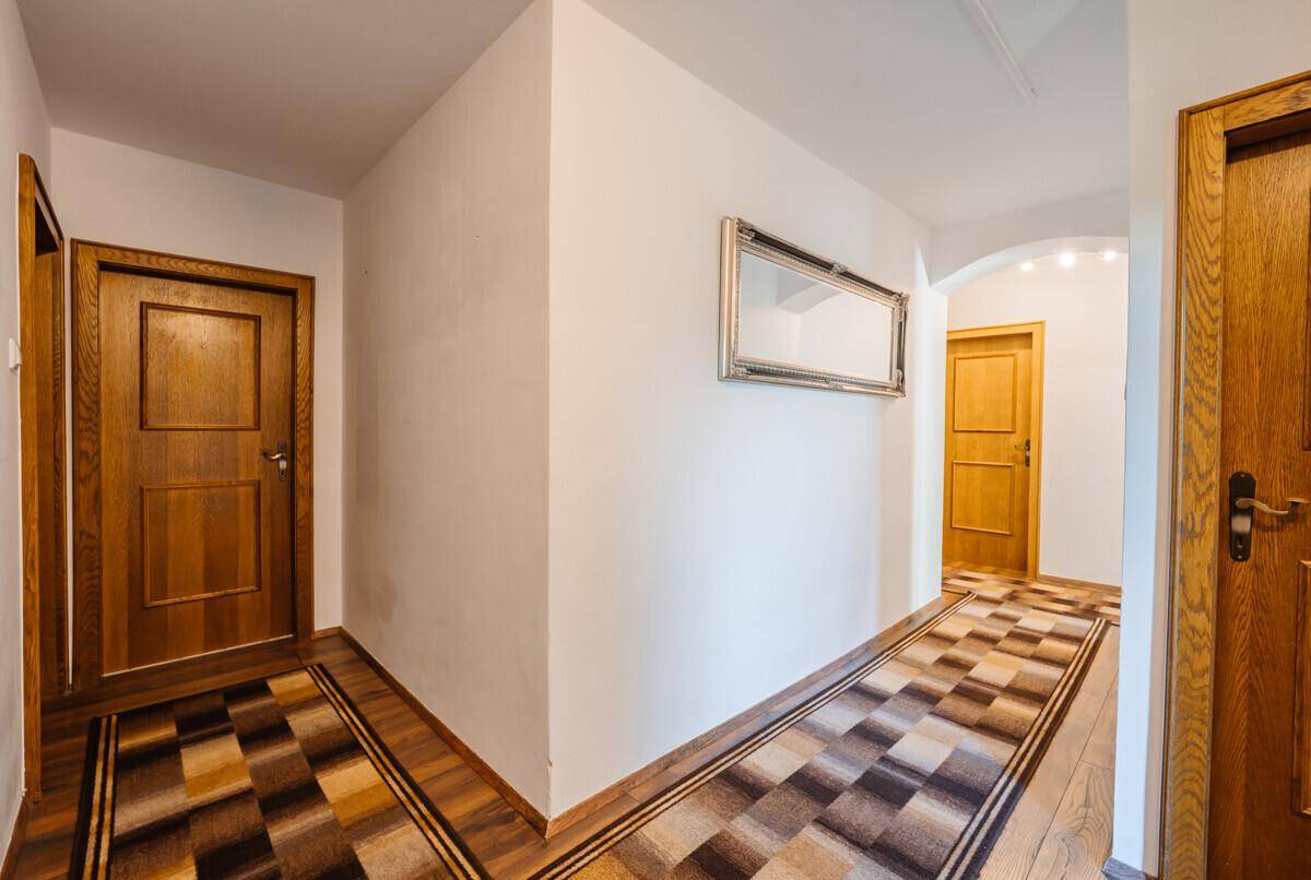 Heller Flur mit Holztüren, gemustertem Teppich und einem Spiegel an der Wand.