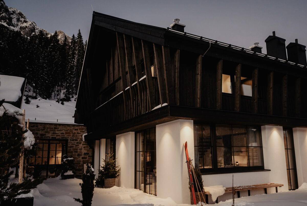 Modernes Chalet im Winter mit verschneiter Umgebung und dunkler Holzfassade.