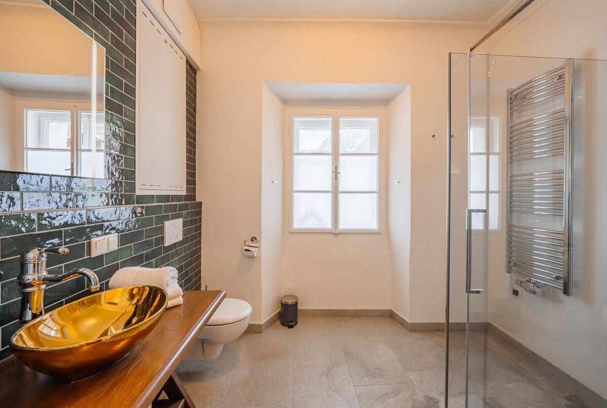 Modernes Badezimmer mit goldener Waschschale, begehbarer Dusche und Fenster für natürliches Licht.