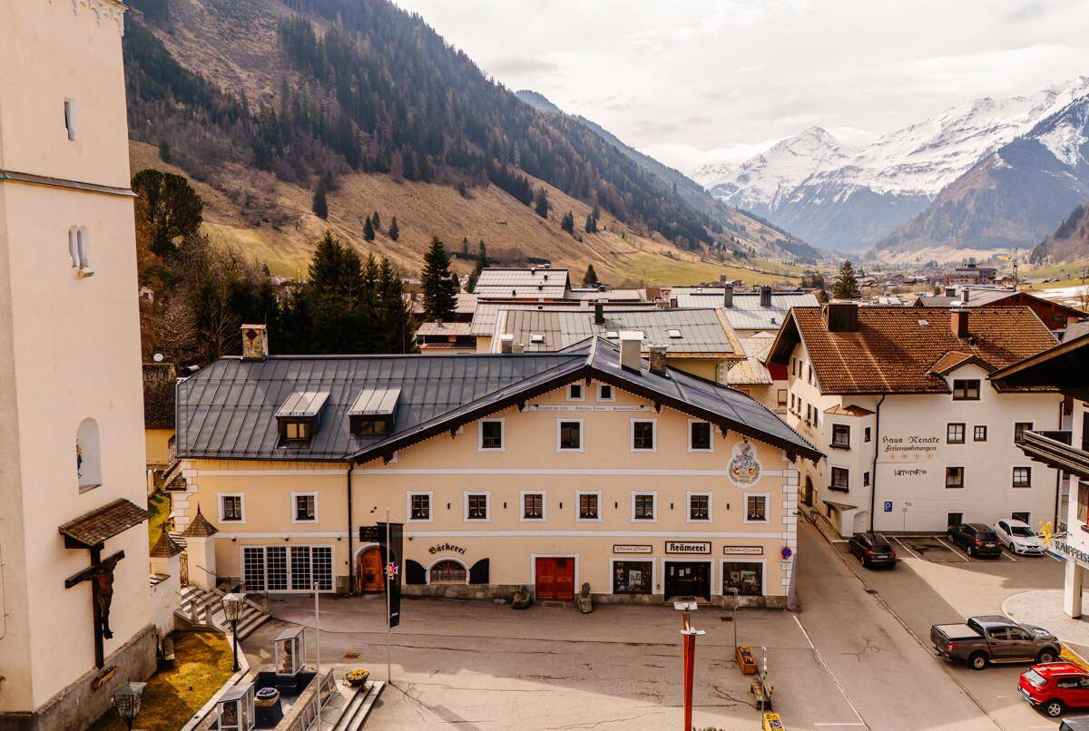 Historisches Gebäude in einem alpinen Dorf mit Bergblick und umliegenden Häusern.