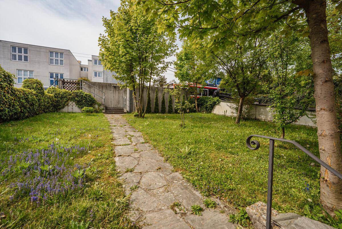 Großer, gepflegter Garten mit Rasenfläche, Steinweg und üppiger Bepflanzung hinter dem Haus.