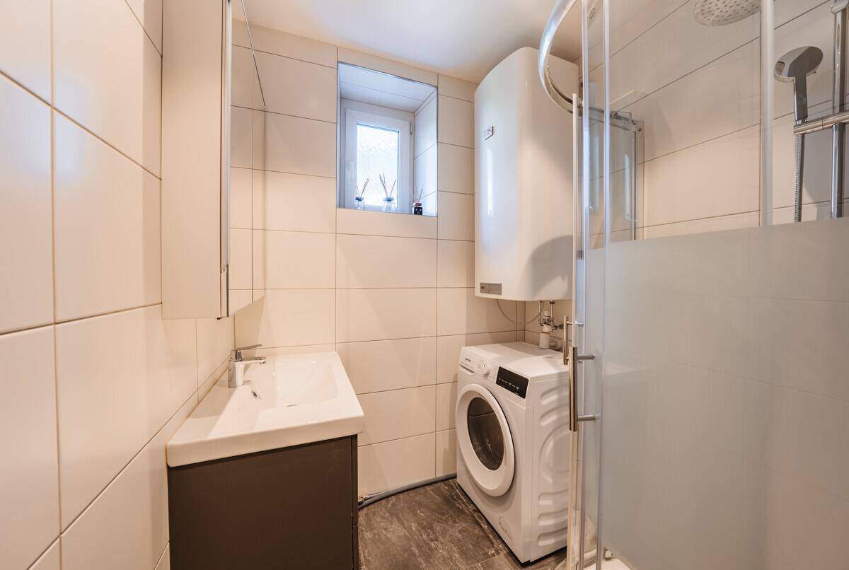 Modernes Badezimmer mit Duschkabine, Waschmaschine und Fenster für Tageslicht.