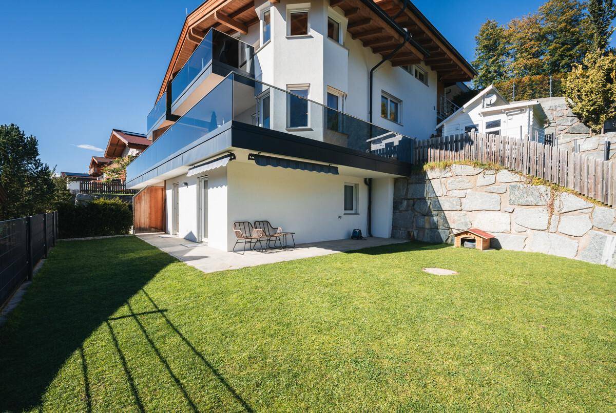 Gepflegter Garten mit Rasenfläche, Terrasse und Blick auf das moderne Wohnhaus.