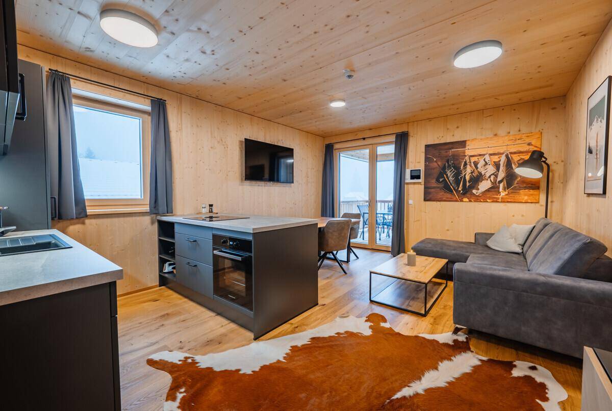 Gemütlicher Wohn-Essbereich mit offener Küche, Holzvertäfelung und Blick auf die verschneite Landschaft.