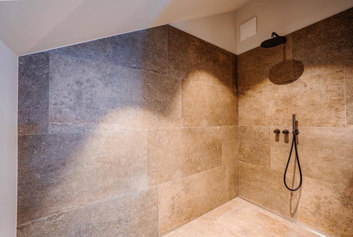 Moderne Dusche mit großformatigen Fliesen und schwarzer Regendusche.