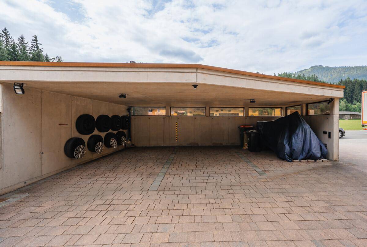 Überdachter Parkplatz mit gepflastertem Boden und Stauraum für Reifen, praktisch und funktional.