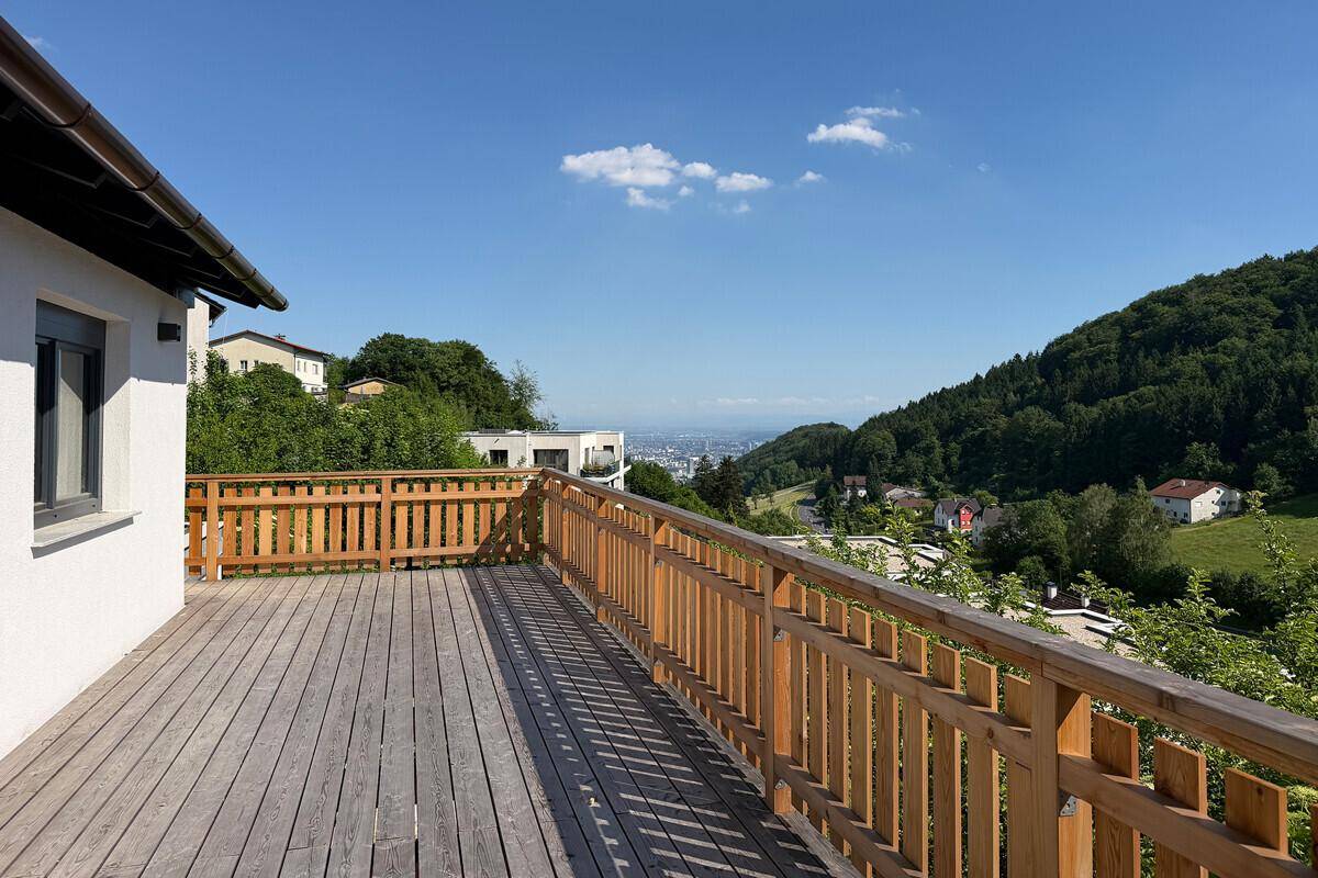 Geräumige Holzterrasse mit Geländer und Panoramablick auf die bewaldeten Hügel und die Stadt in der Ferne.