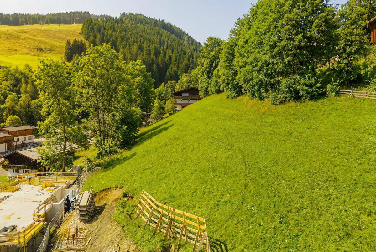 Grüne Hügellandschaft mit einer Baustelle im Vordergrund und traditionellen Gebäuden im Hintergrund.