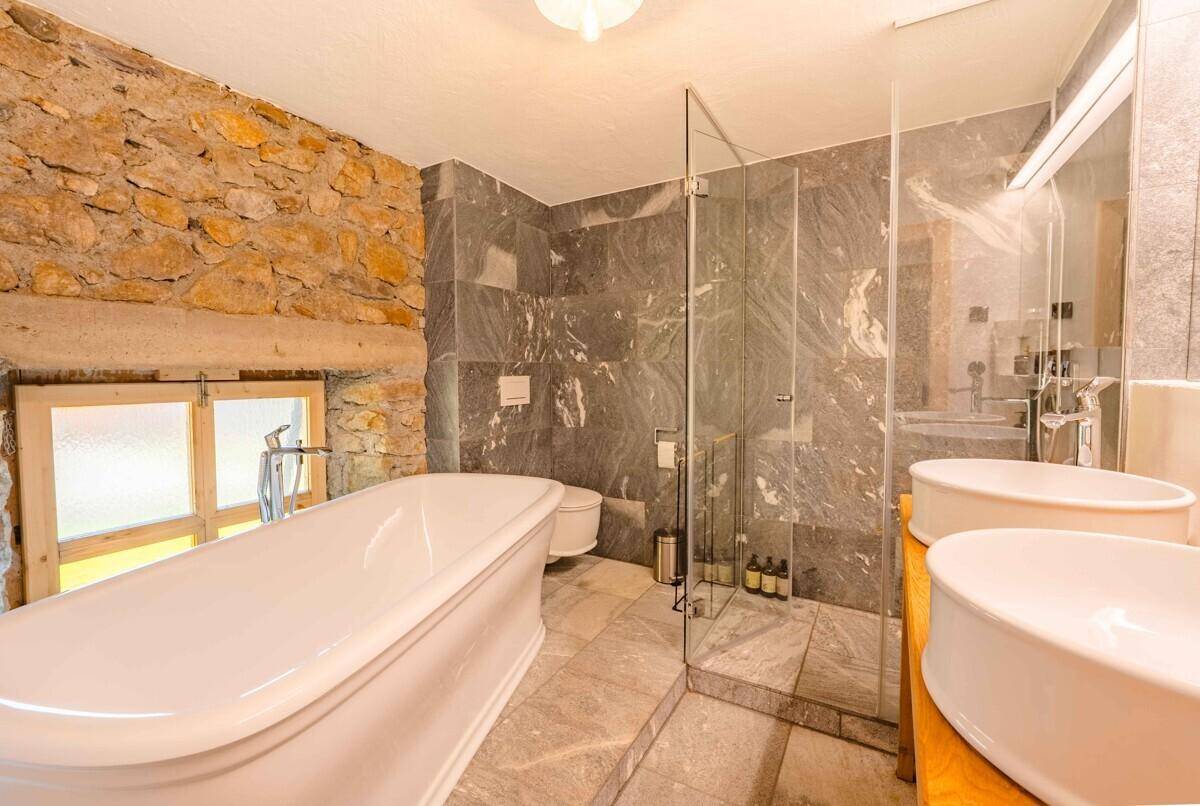 Modernes Badezimmer mit freistehender Badewanne, begehbarer Dusche und Steinwänden.