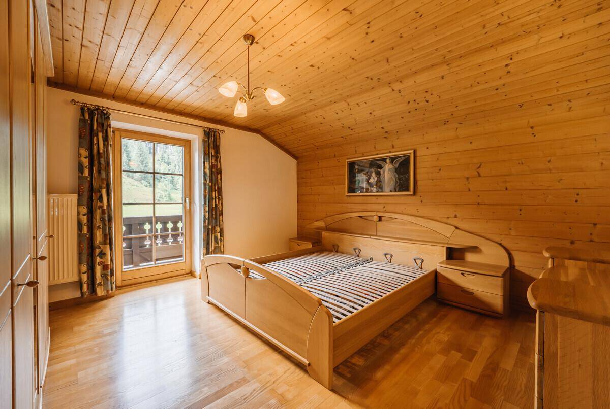 Gemütliches Schlafzimmer mit Holzwänden, Holzdecke und Zugang zu einem Balkon.