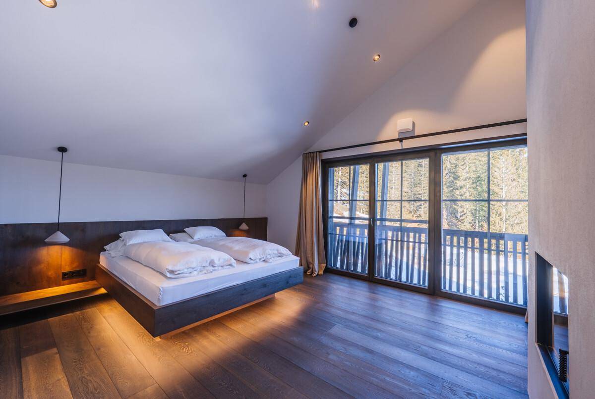 Helles Schlafzimmer mit Holzboden, schwebendem Bett und Zugang zum Balkon mit Bergblick.