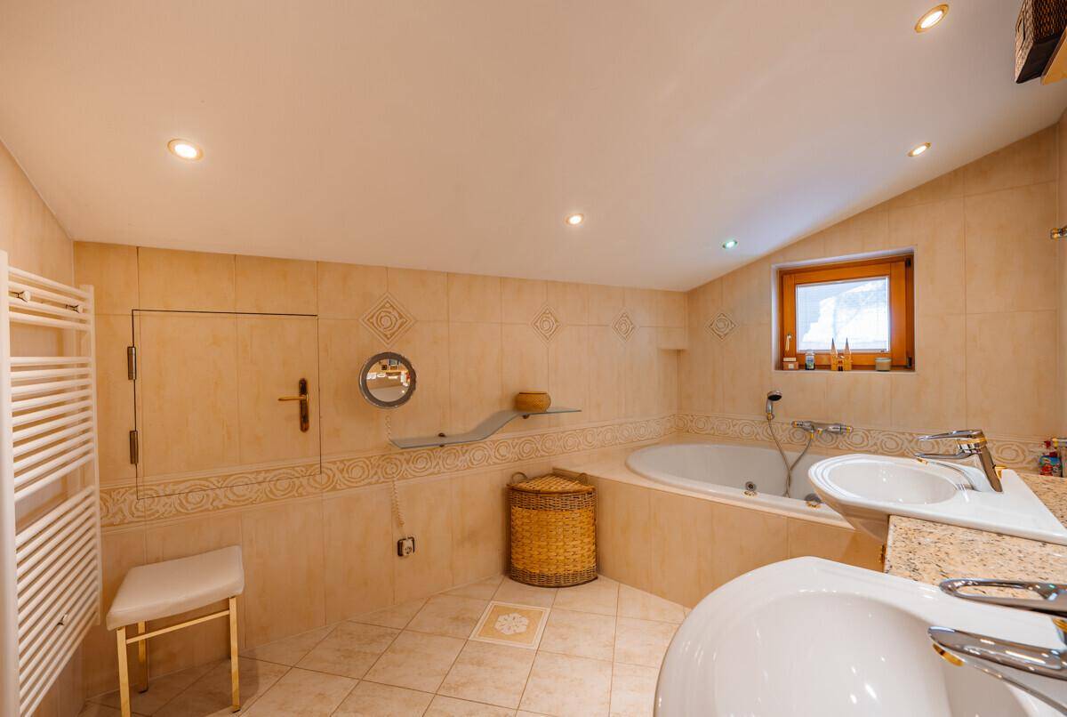 Badezimmer mit beigen Fliesen, Eckbadewanne, Doppelwaschbecken und einem Fenster.