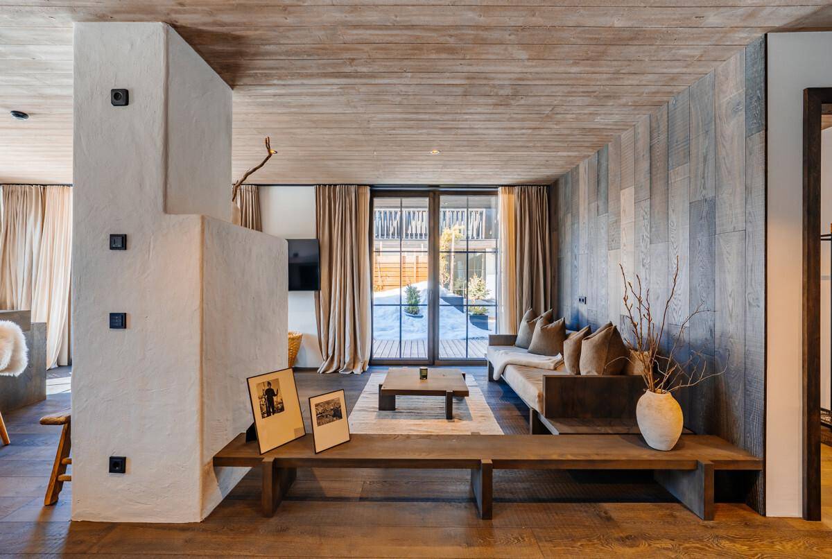 Gemütliches Wohnzimmer mit Holzboden, Kamin und Blick auf die verschneite Landschaft.
