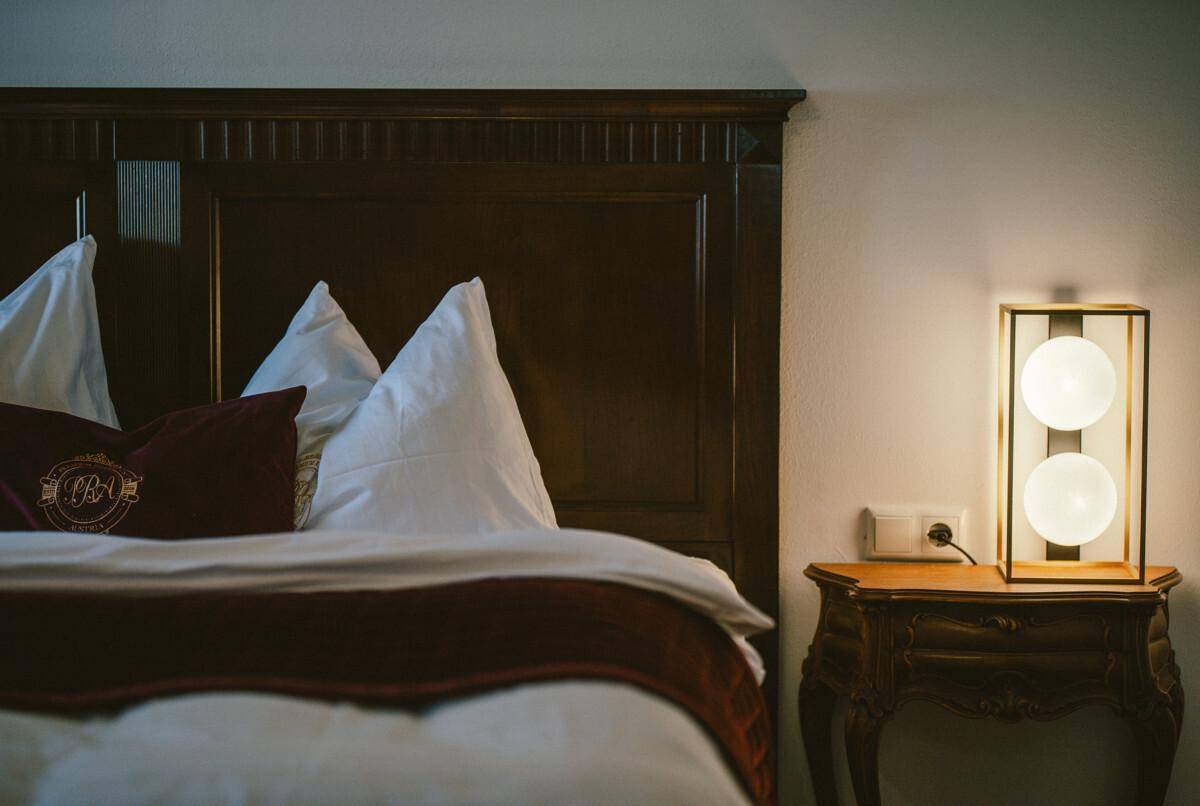 Detailansicht des Holzbettes mit Nachttisch und moderner Lampe.