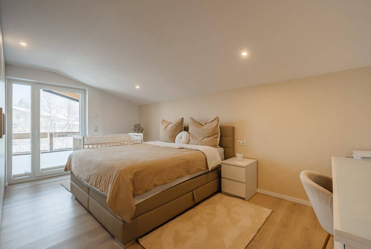 Helles Schlafzimmer mit Doppelbett, Babybett und Zugang zu einem Balkon.