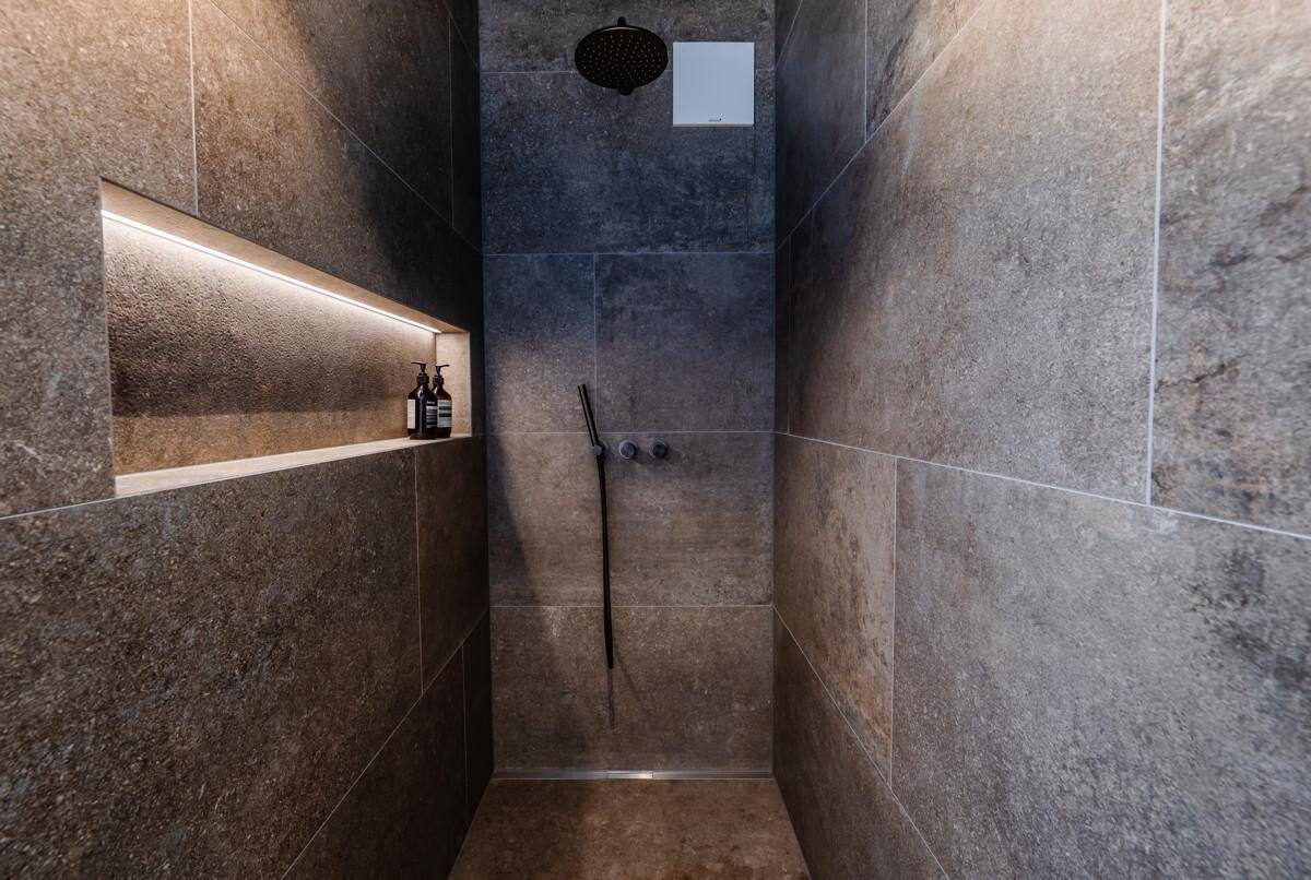Moderne Dusche mit großformatigen Fliesen, integrierter Nische und Regenduschkopf.