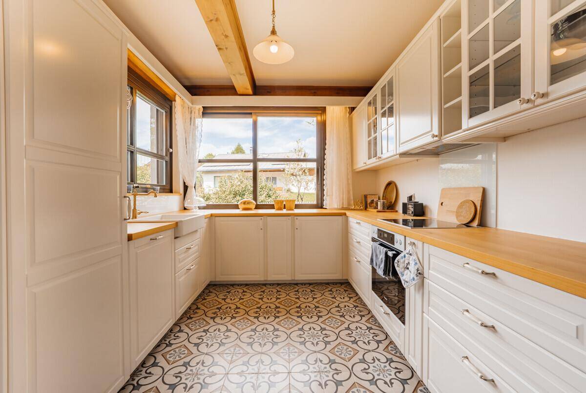 Helle Küche im Landhausstil mit Holzarbeitsplatten, gemusterten Fliesen und Fensterblick.