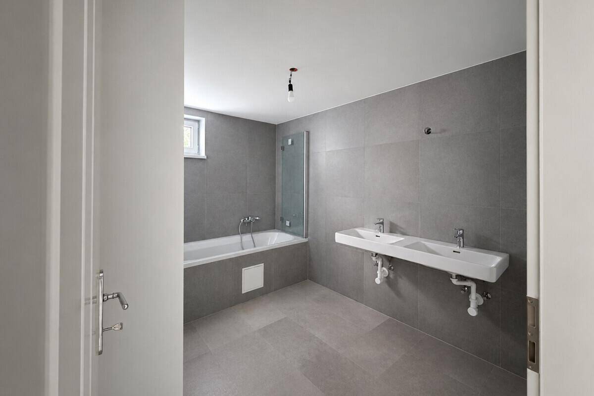 Modernes Badezimmer mit grauen Fliesen, Badewanne und Doppelwaschbecken, bereit für die Endmontage.