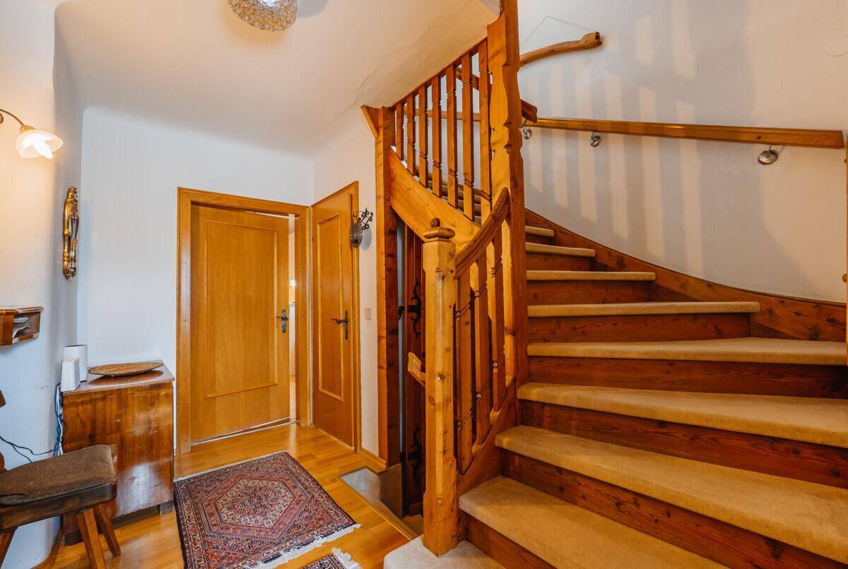 Eingangsbereich mit einer geschwungenen Holztreppe und traditionellen Holztüren, die einladend wirken.