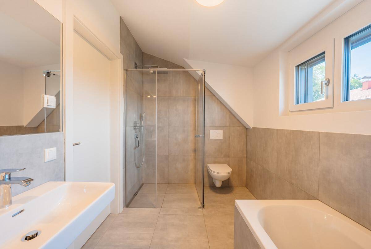 Modernes Badezimmer mit Dusche, WC, Waschbecken und Badewanne unter einer Dachschräge mit Fenster.