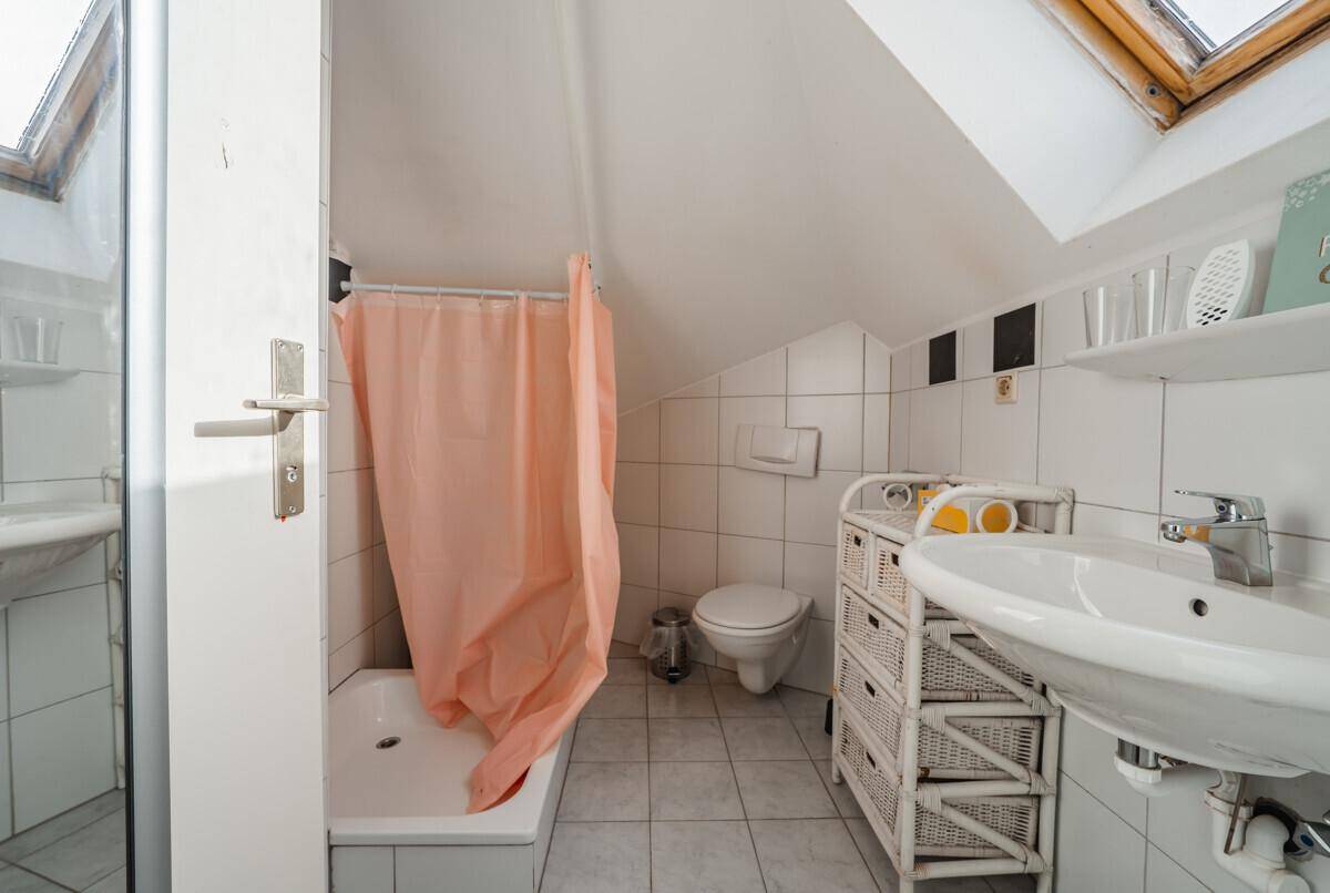 Dachgeschoss-Badezimmer mit Badewanne, WC, Waschbecken, Fliesenboden und Dachfenster.