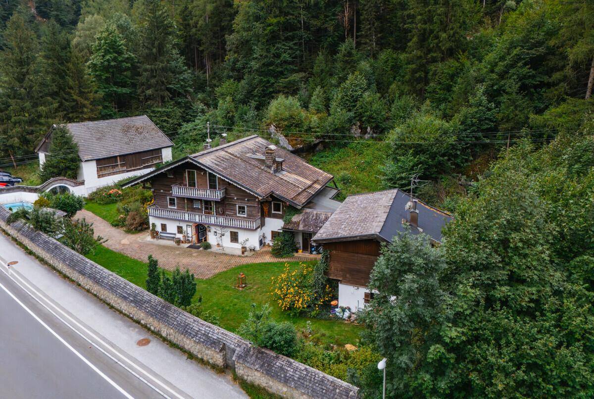 Luftaufnahme des Anwesens mit mehreren Gebäuden, umgeben von dichtem Wald und einer Straße.