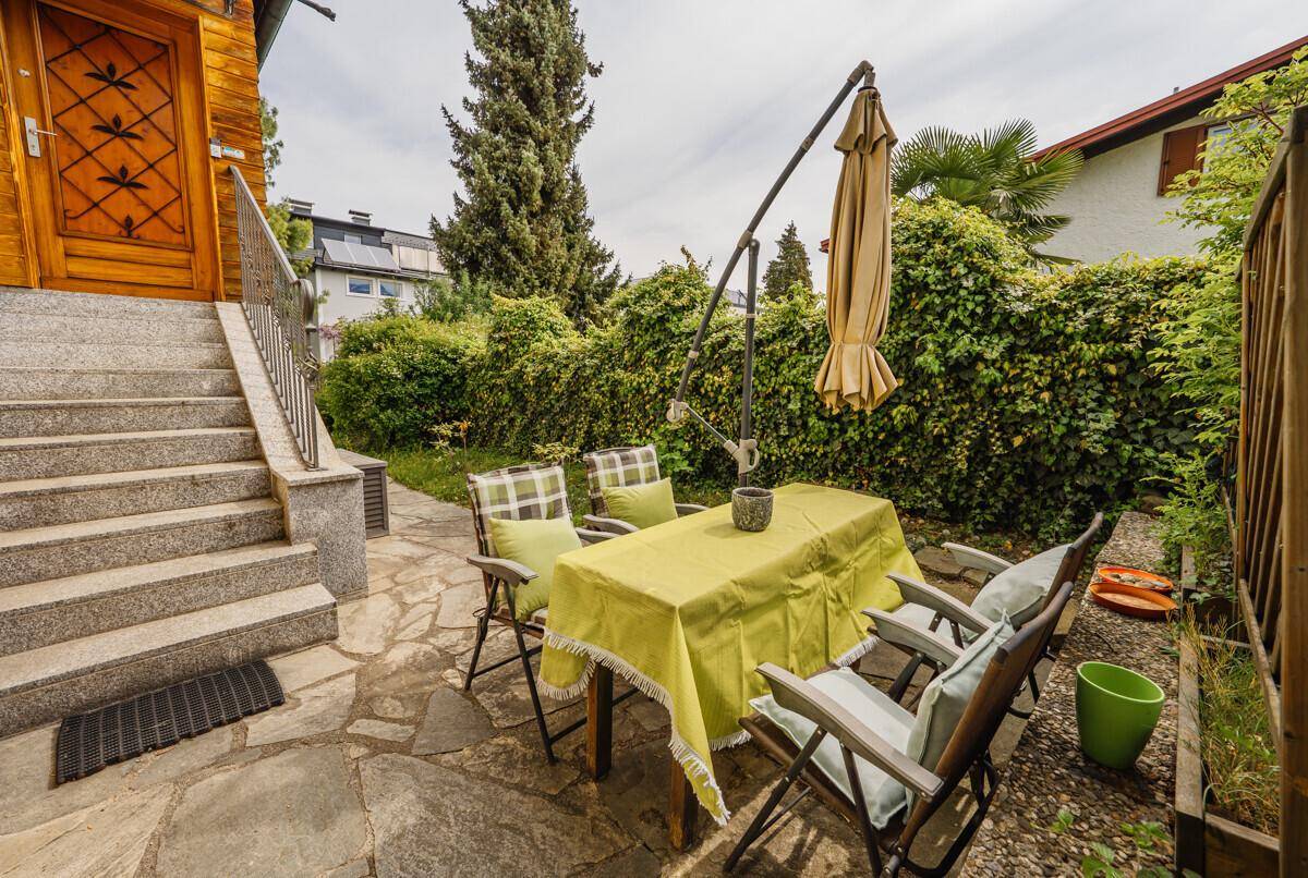 Gemütliche Steinterrasse mit Gartenmöbeln und Sonnenschirm, umgeben von grünen Hecken.