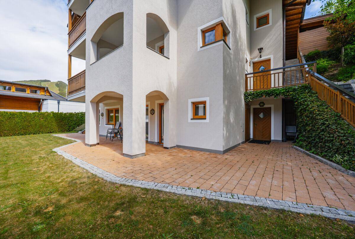 Moderne Fassade mit gewölbten Bögen, einer gepflasterten Terrasse und einem grünen Rasenbereich.