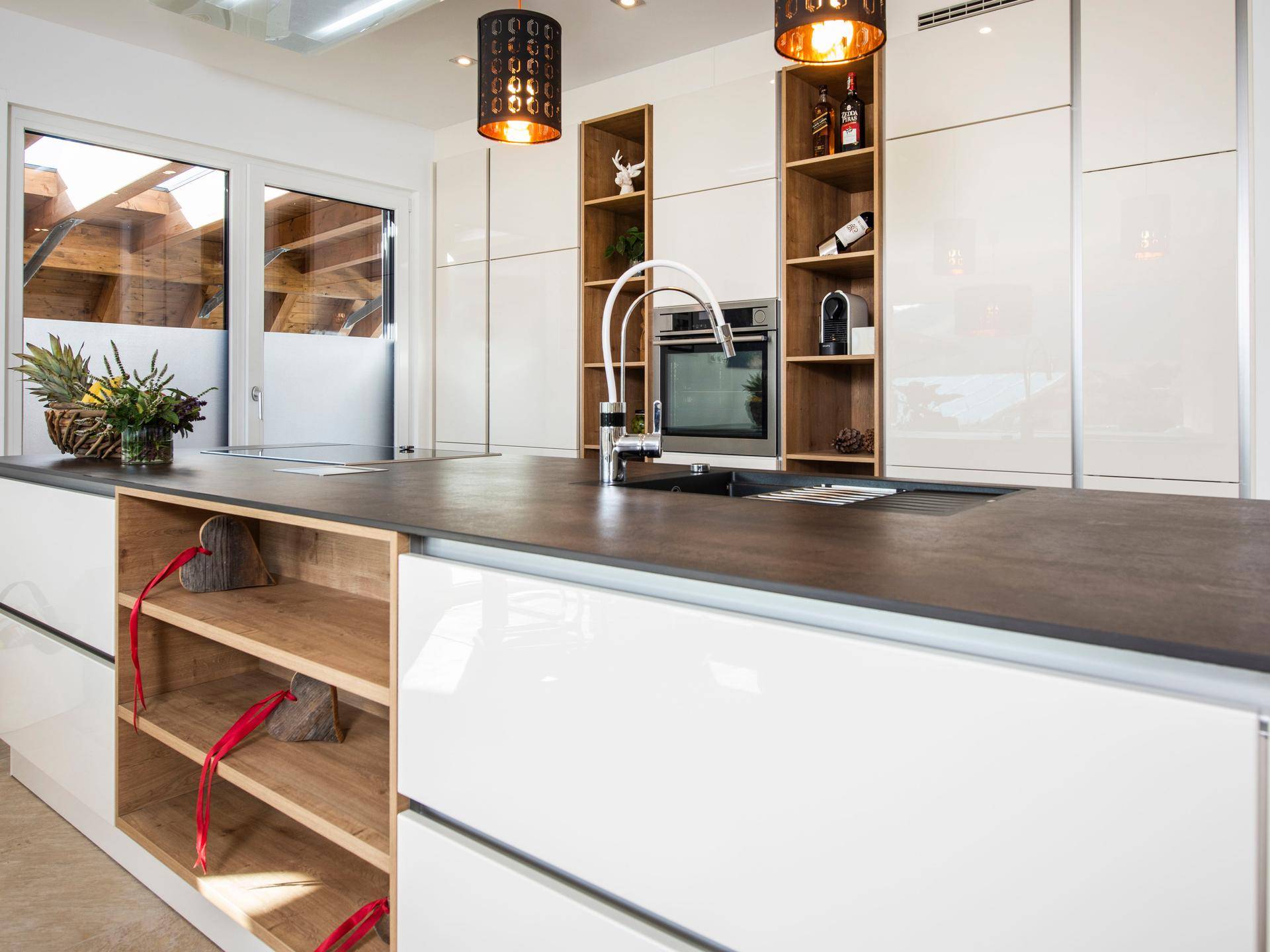 Moderne Küche mit weißen Hochglanzfronten, dunkler Arbeitsplatte und integrierten Geräten.