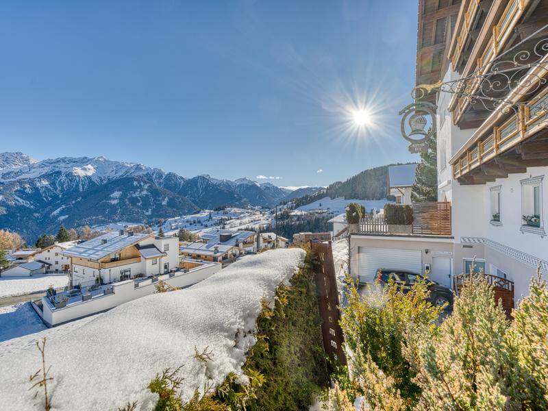 Sonniger Ausblick von einem Balkon auf die verschneite Berglandschaft und die umliegenden Gebäude.