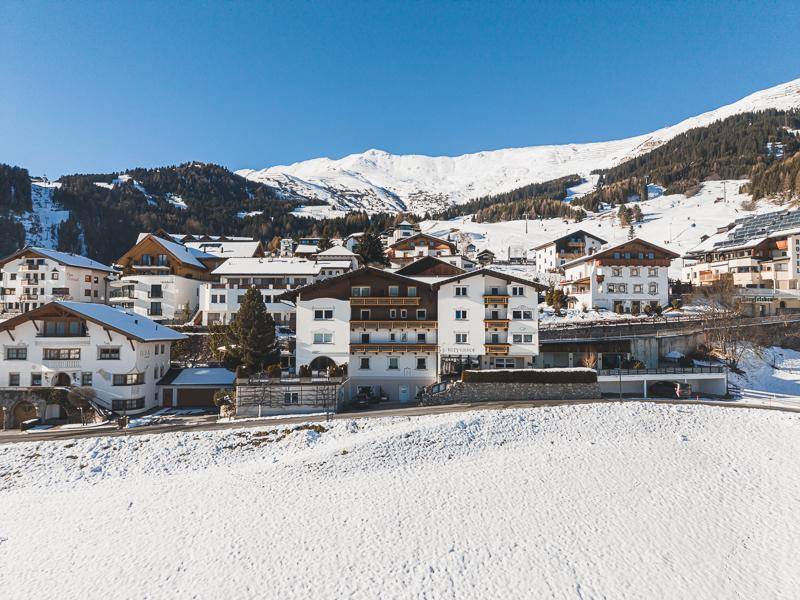 Mehrere Gebäude im alpinen Stil in einer verschneiten Berglandschaft unter blauem Himmel.