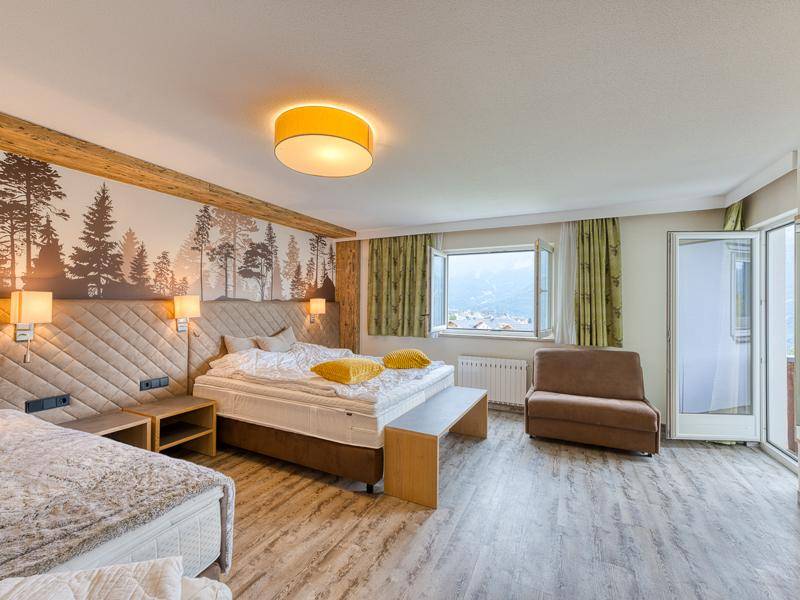 Helles Schlafzimmer mit zwei Betten, Holzelementen und weitem Blick auf die umliegende Berglandschaft.