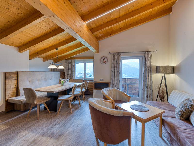Geräumiger Wohn- und Essbereich mit beeindruckender Holzbalkendecke und Zugang zum Balkon mit Bergblick.