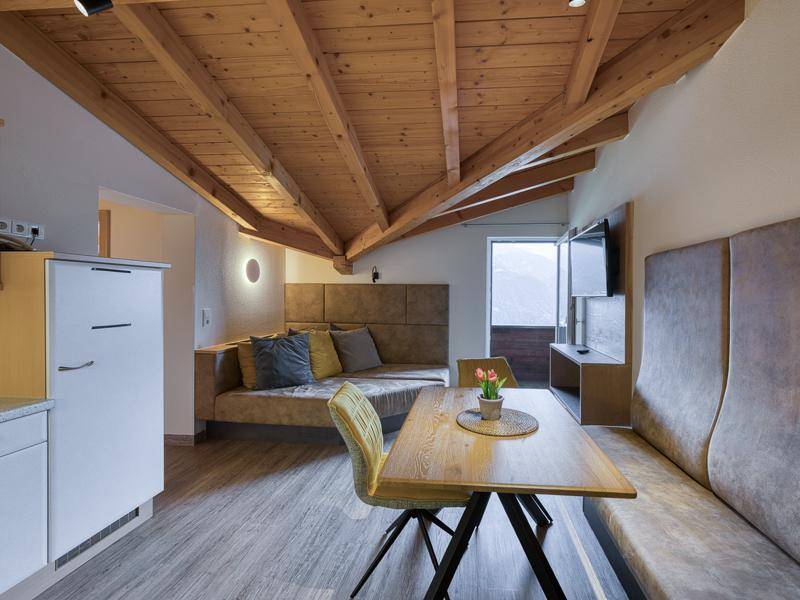 Offener Wohn- und Essbereich mit Holzbalkendecke, kleiner Küchenzeile und Bergblick.