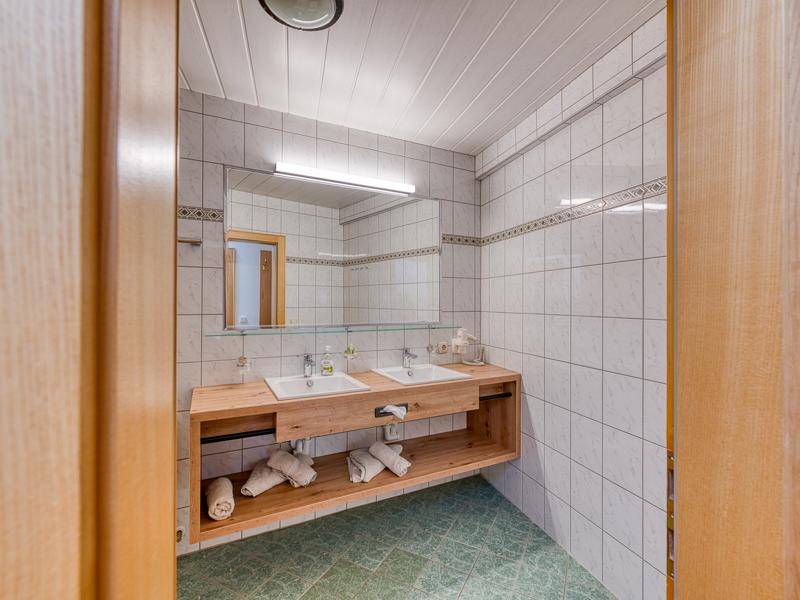 Funktionales Badezimmer mit Doppelwaschbecken, Holzunterschrank und hellen Fliesen an den Wänden.