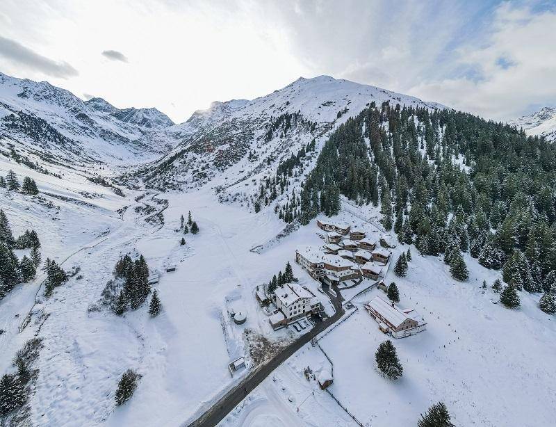 Luftaufnahme einer Ferienanlage in einer verschneiten Berglandschaft mit vielen Chalets.
