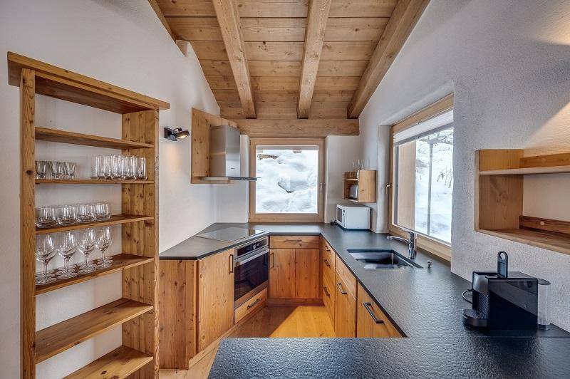 Moderne Holzküche mit dunkler Arbeitsplatte, integrierten Geräten und Blick auf die verschneite Landschaft.