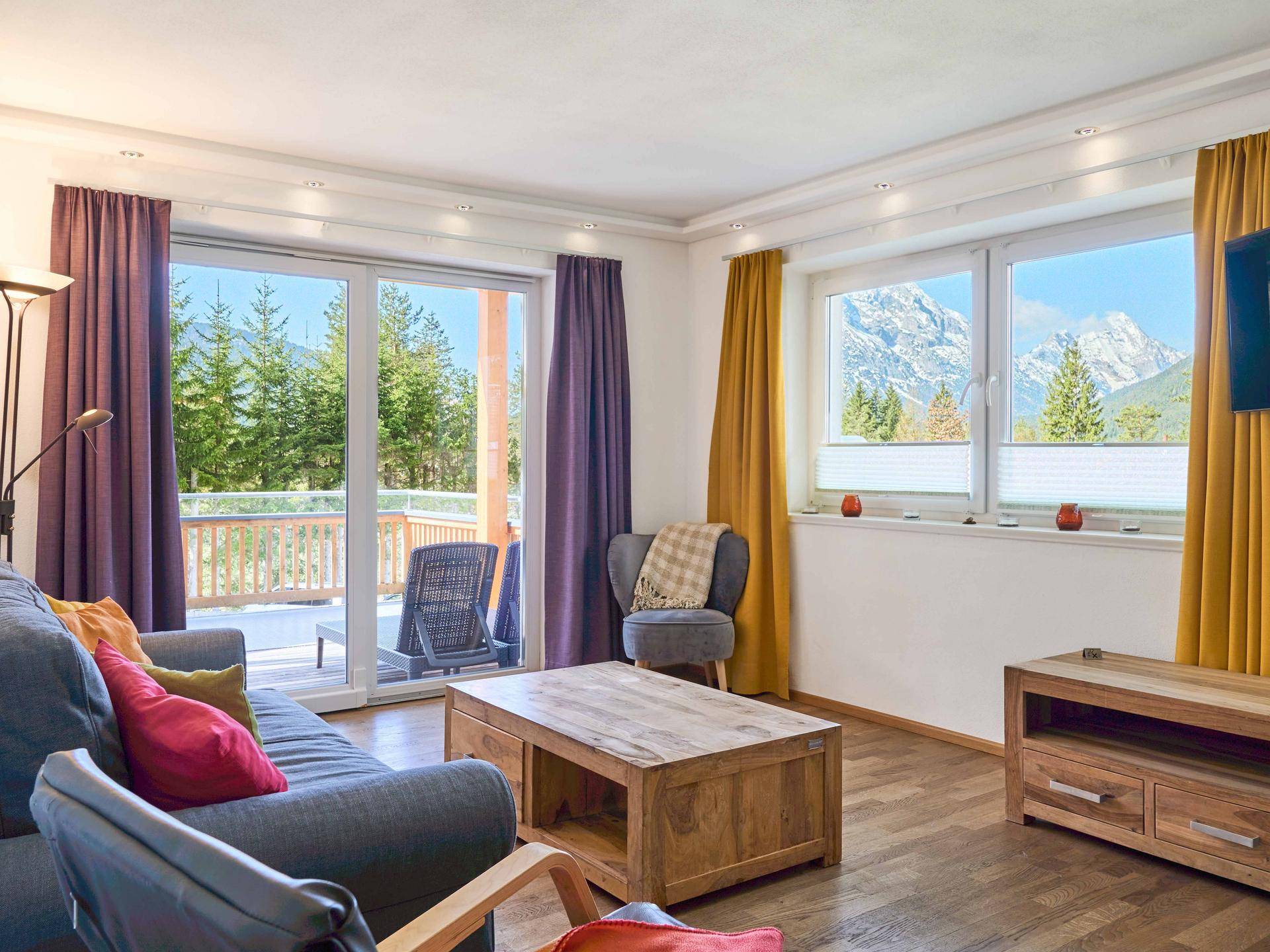 Helles Wohnzimmer mit gemütlichem Sofa, Holztisch und Zugang zu einem Balkon mit Bergblick.