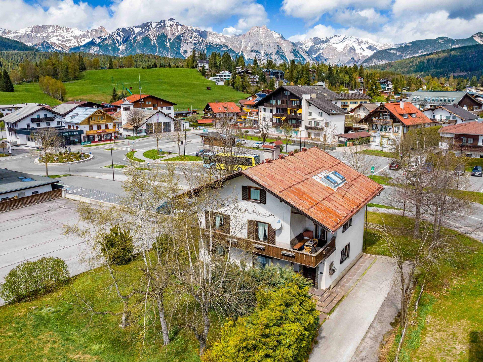 Haus mit Balkon in einer Berglandschaft, umgeben von weiteren Gebäuden und grünen Hügeln.