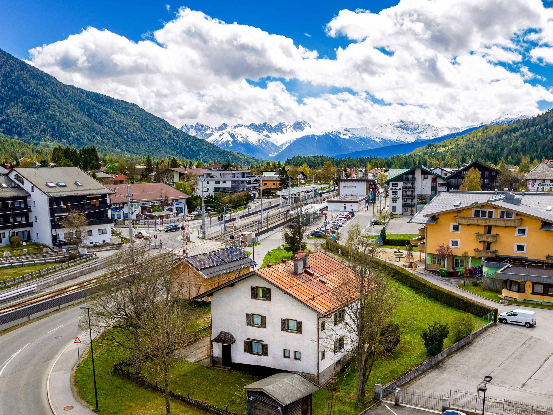 Panoramablick auf ein Dorf in den Alpen mit Bahnhof und schneebedeckten Bergen im Hintergrund.