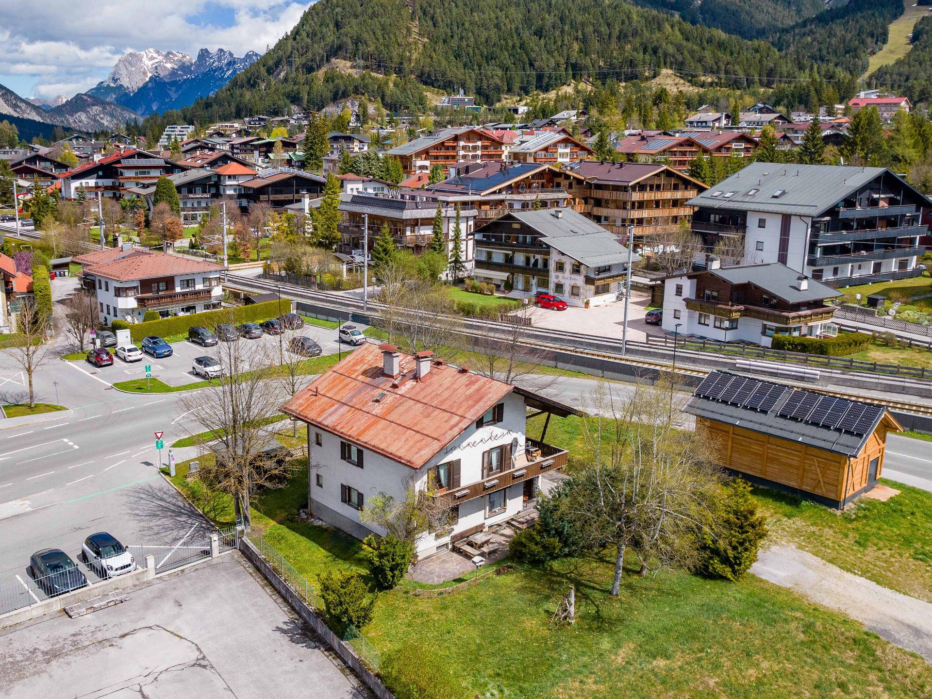 Haus mit Balkon in alpiner Umgebung, nahe einer Bahnlinie und umgeben von weiteren Gebäuden.