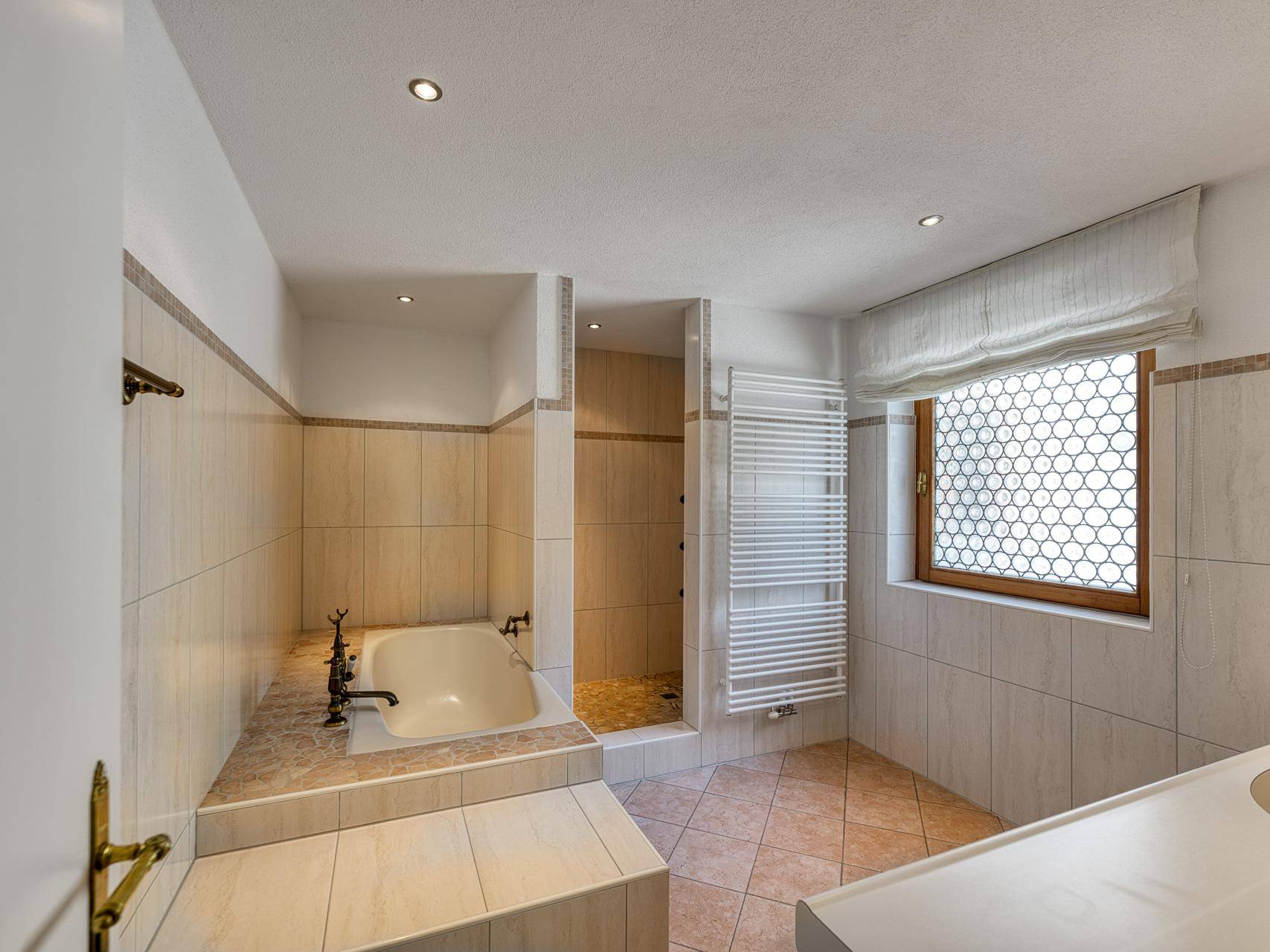 Badezimmer mit Badewanne, Duschbereich, Fliesenboden und beheiztem Handtuchhalter.