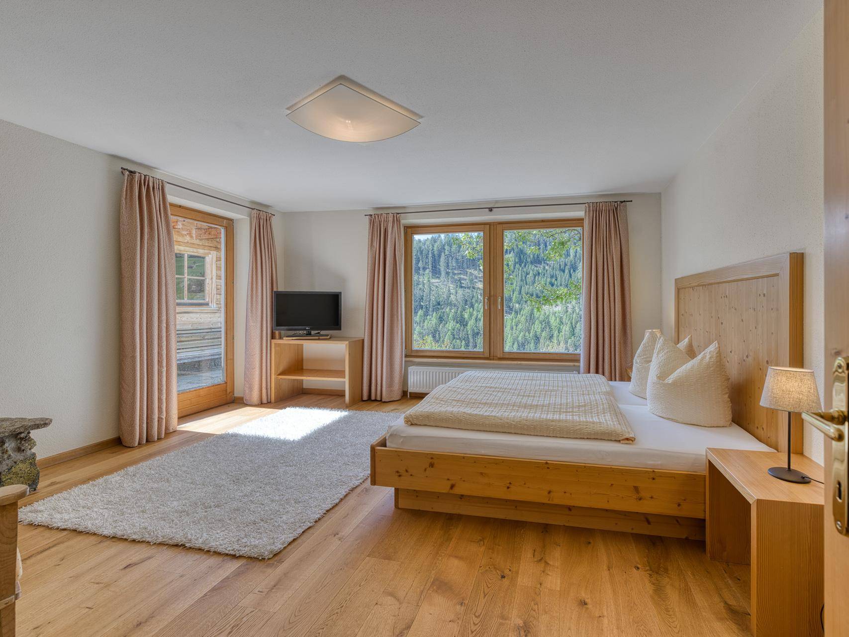 Helles Schlafzimmer mit Holzbett, Parkettboden und direktem Zugang zu einem Balkon mit Waldblick.