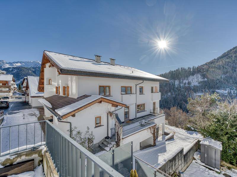 Alpines Haus in verschneiter Landschaft mit Bergblick unter strahlend blauem Himmel.