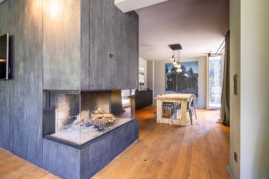 Moderner Kamin als Raumteiler zwischen Wohn- und Essbereich mit Holzboden und Kunstwerken.